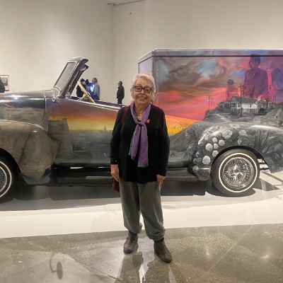 Photograph of Carol Jacques standing in front of a vintage car with a mural on its side